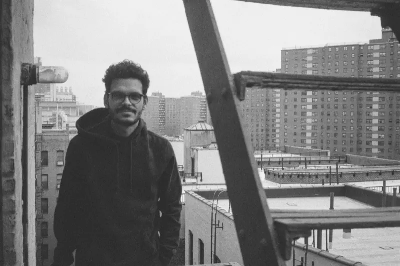 Lucas on a fire escape with city rooftops behind